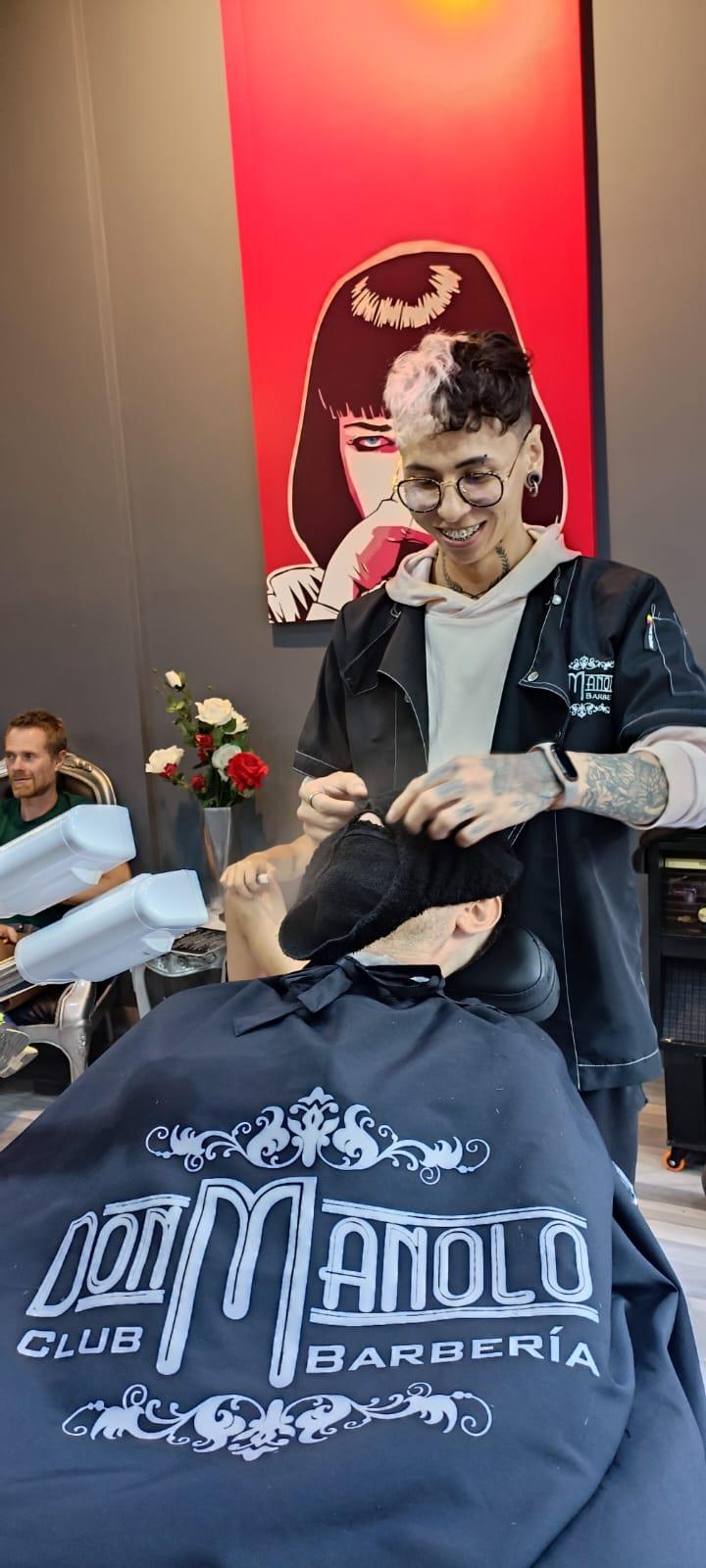 Barbero colocando toalla caliente a un cliente con la capa del logo Don Manolo